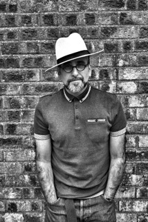 Composer Julio d'Escriván standing against a brick wall.